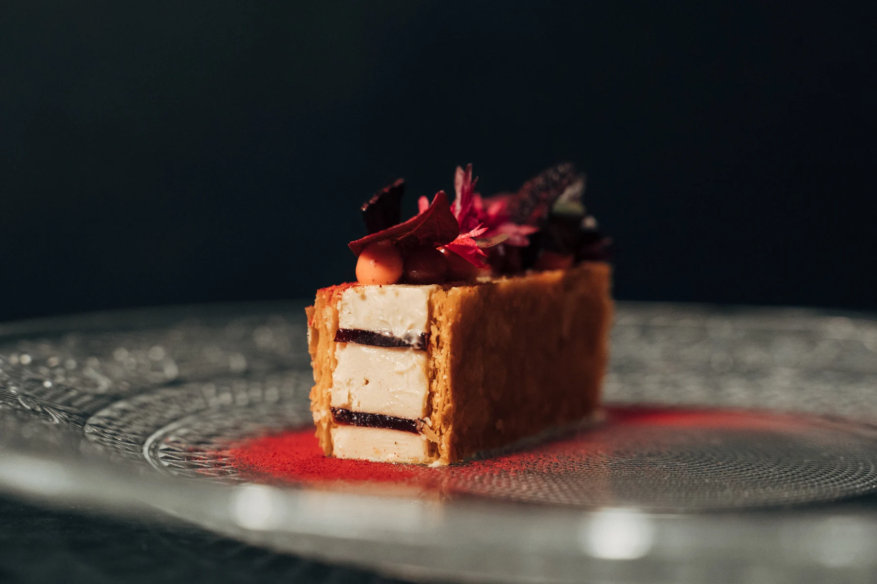 Feines geschichtetes Dessert mit roten Blüten auf einem Glasteller